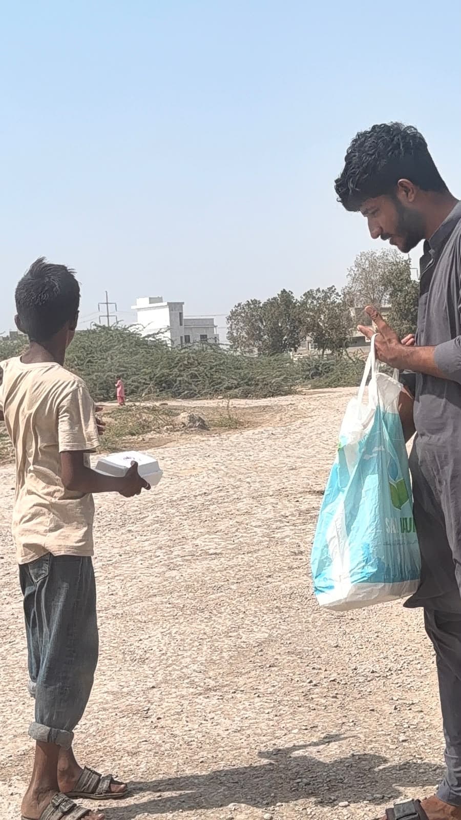A volunteer reaching into a bag of meals while a boy holds the box he was given